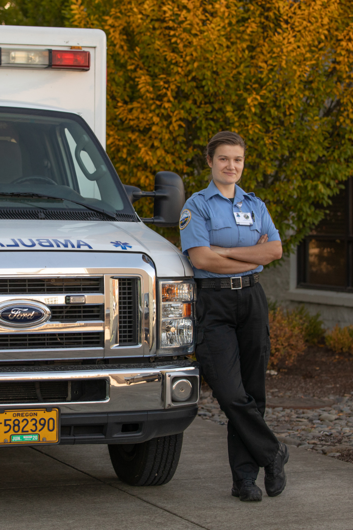 An EMT student posing against the side of an ambulance